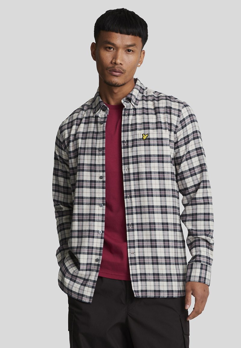 Geruite overhemdd in wit, marineblauw en bordeaux, gelaagd over een bordeaux t-shirt. Kenmerkend is een klein geel geborduurd logo op het shirt.