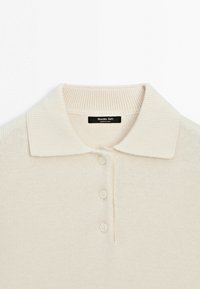 Gestricktes Poloshirt in Off-White, mit flachem Kragen, drei Knöpfen und einem strukturierten Stoff mit dezentem Rippenmuster.