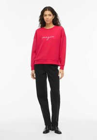 Červená mikina s bílým nápisem "imagine", objemný střih, kulatý výstřih, doplněná černými džíny s rovnými nohavicemi a černými kotníkovými botami.