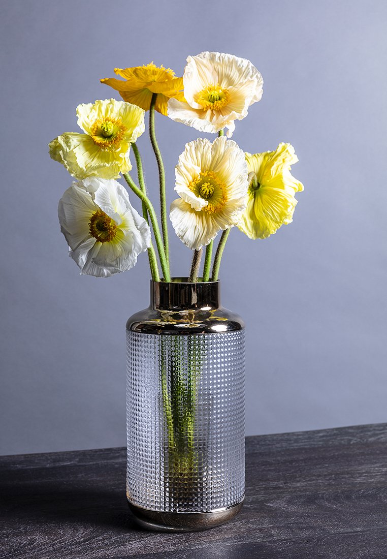 Klare Glasvase mit strukturierter Oberfläche und metallisch goldenem Rand. Enthält sechs Blumen: gelbe und weiße Mohnblumen mit ausgeprägten, geschichteten Blütenblättern.