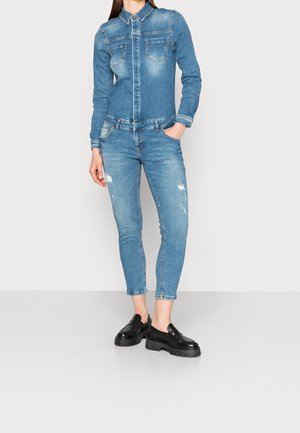 Denimjakke med lange ærmer, to brystlommer og falmet blå farve, kombineret med blå skinny jeans med slidte detaljer. Sorte sko.