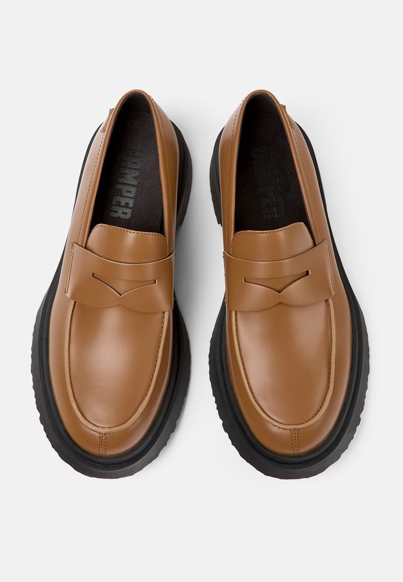 Brązowe skórzane mokasyny o smukłym kształcie, z podwyższonym szwem i czarną gumową podeszwą. Wkładka o fakturowanej powierzchni z widocznym logo marki.