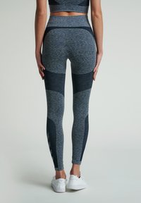 Högmidjade leggings i ett grått och mörkblått mönster. Tillverkade av ett strukturerat, elastiskt material med en smickrande passform och kontrasterande paneler.