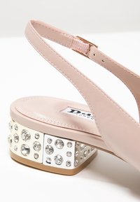 Chaussure slingback en cuir beige avec un petit talon bloc ornée de strass clairs de différentes tailles.