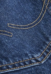 Un tissu en denim d'une teinte bleu profond présente des coutures dorées contrastantes en lignes courbes, mettant en valeur la texture et le savoir-faire du matériau.