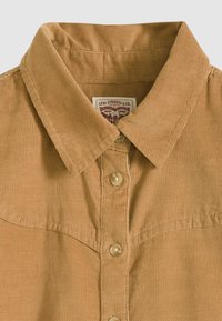 Corduroy shirt in light brown with a classic collar, front button closure, and a textured surface. Label visible at the neckline.