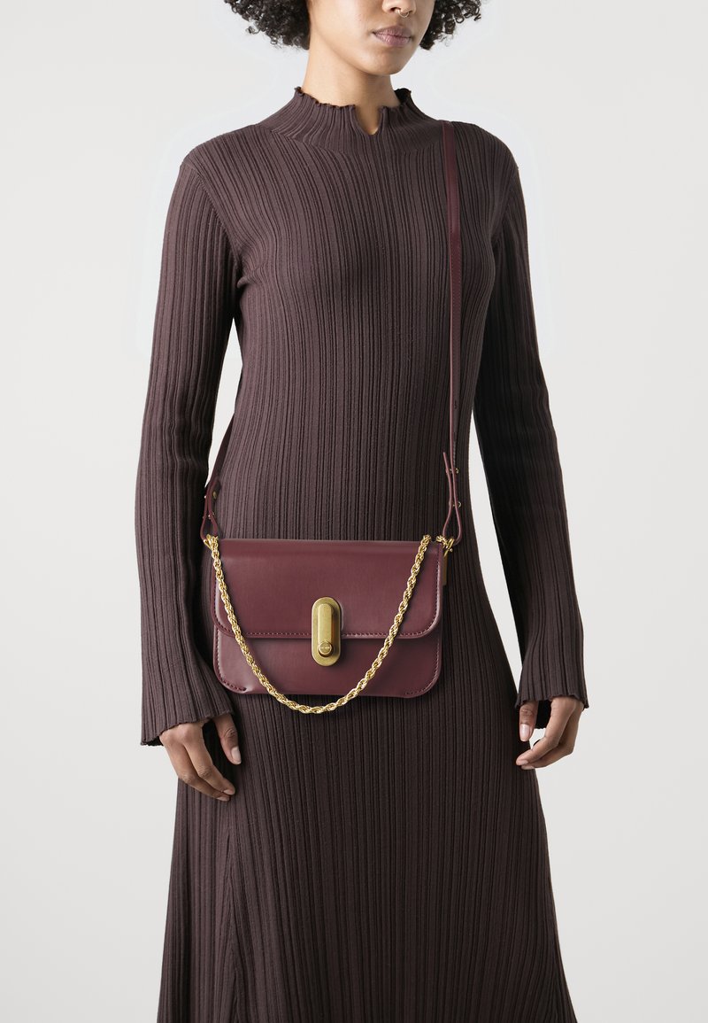 Borsa a tracolla in pelle marrone con una tracolla in catena d'oro, forma rettangolare e superficie liscia. Presenta una chiusura decorativa sul fronte.