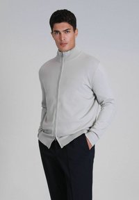 Lichtgrijze zip-up sweater met een staande kraag, een getailleerd ontwerp en een geribbelde textuur, gecombineerd met donkere broek.