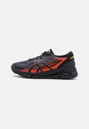 Zapatilla de running para hombre con parte superior negra con patrones geométricos rojos, suela negra y acentos amarillos en la lengüeta, diseñada para el rendimiento.