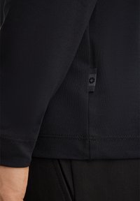 Tessuto nero e strutturato di una camicia aderente con maniche corte, dotata di un'etichetta logo vicino all'orlo e un design senza cuciture ai polsini.