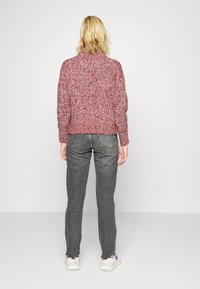 Strickpullover in gemischtem Pink und Burgunder, strukturierter Stoff, runder Ausschnitt, kombiniert mit grauen gerade geschnittenen Jeans und weißen Turnschuhen.