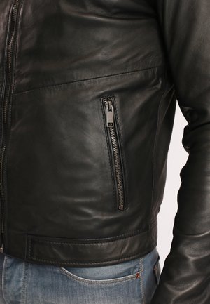 Giubbotto in pelle nera con un design aderente, dotato di una tasca con zip sul lato sinistro e una texture liscia. Accentuato con accessori in metallo argentato.