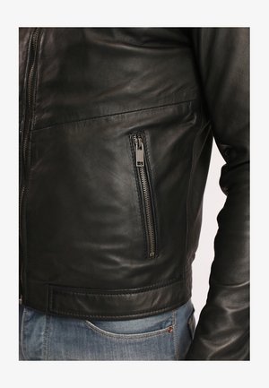 Giubbotto in pelle nera con un design aderente, dotato di una tasca con zip sul lato sinistro e una texture liscia. Accentuato con accessori in metallo argentato.