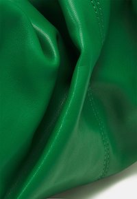 Grön läderväska med mjuk textur, som visar veck och söm detaljer. Har en glänsande yta och en voluminös form.