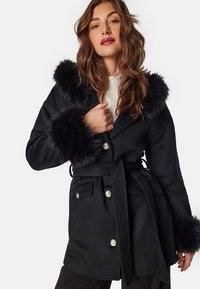 Black wool coat with a faux fur hood and cuffs, featuring a wrap design, two front pockets, and silver button accents.