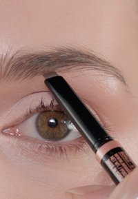 Brauner Augenbrauenstift mit feiner Spitze, schwarzem Gehäuse und pinkem Akzent. Aufgenommen in einer Nahaufnahme der Haut in der Nähe eines braunen Auges mit langen Wimpern.