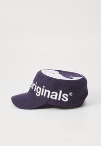 Lilla bomullslue med flat skygge, som har en fremtredende hvit logo og grafikk på toppen. Teksturen ser glatt ut og stoffet ser slitesterkt ut.