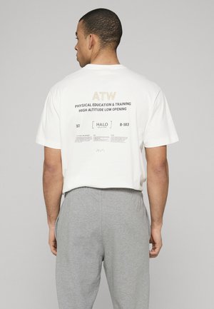 Wit katoenen T-shirt met zwarte en gouden tekstprint op de rug. Het ontwerp bevat logo's en contouren in een minimalistische stijl.