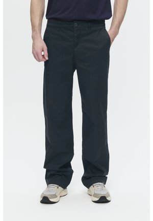 Dark navy cotton trousers with a straight cut, featuring a button closure and front pockets, paired with light-colored sneakers.