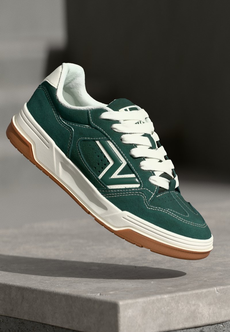 Green suede sneaker with white accents, round toe, and flat laces; features a textured rubber sole and side vent accents.