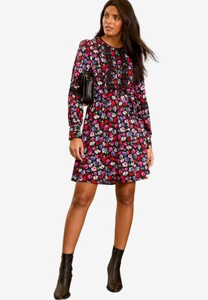 Floral dress in black with red, pink, and purple flowers; long sleeves, cinched waist, paired with a black handbag and ankle boots.
