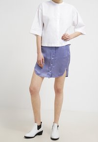 Vit kortärmad cropped skjorta, matchad med en blå rutig kjol med framknappar och sidospalter. Svart och vit ankelboots.