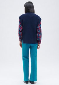 Meripihkan bersatu rajutan navy di atas kemeja lengan panjang bermotif kotak-kotak dalam nada biru dan burgundy, dipadukan dengan celana lurus turquoise dan sepatu hitam.