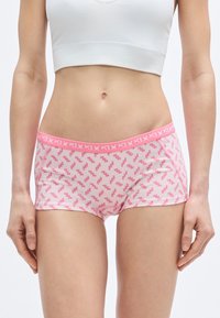 Ροζ σορτς με ζιγκ-ζαγκ σχέδιο, κατασκευασμένα από απαλό ύφασμα. Η ζώνη μέσης είναι ανοιχτό ροζ με αντίθετο λογότυπο της μάρκας σε λευκό.
