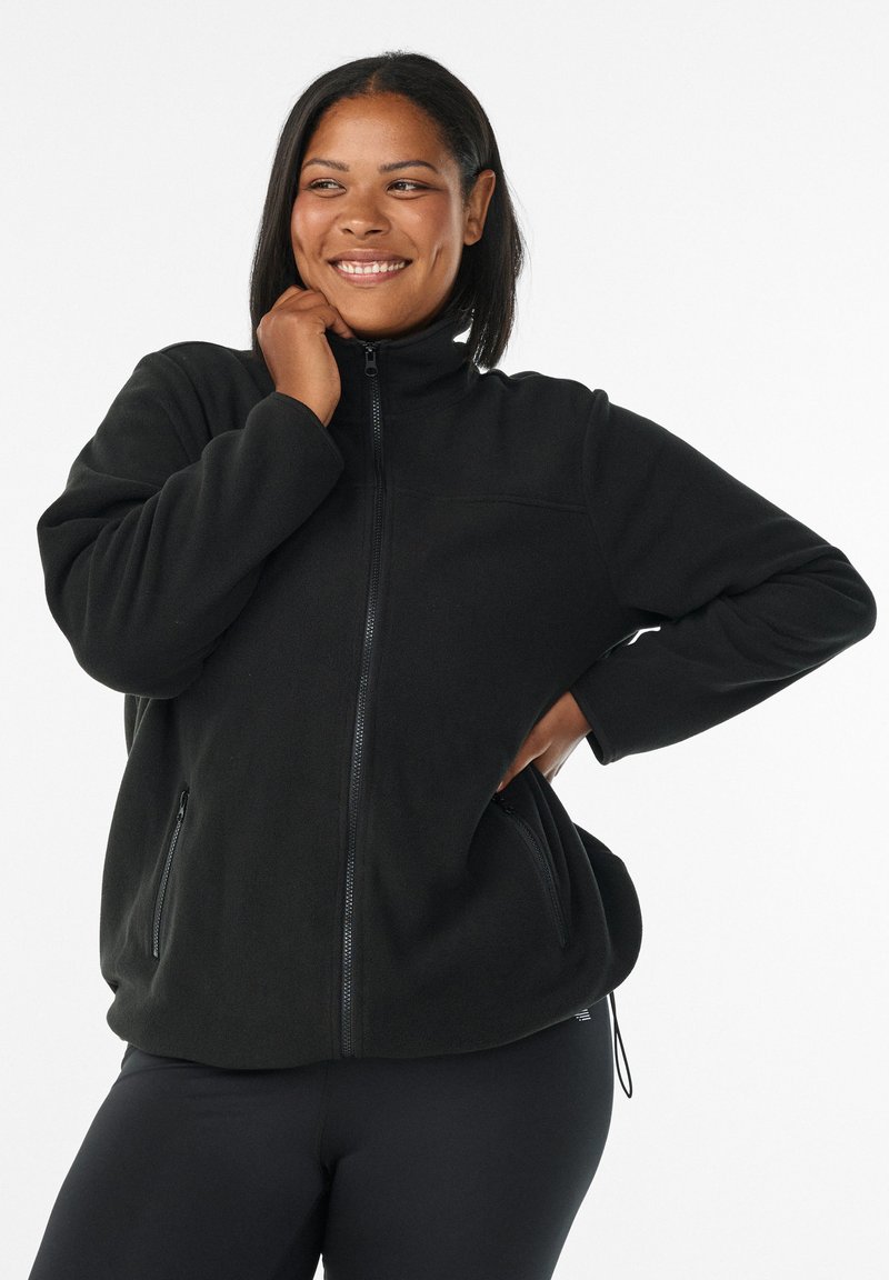 Veste en polaire noire avec col haut, fermeture éclair complète et deux poches latérales. Présente une coupe décontractée et une texture douce.