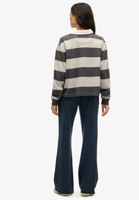 Pasiasty pulower w odcieniach szarości z białym kołnierzykiem i luźnym krojem, zestawiony z granatowymi rozszerzanymi spodniami. Miękka tkanina o swobodnym designie.