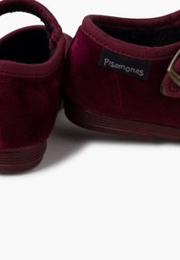 Zapatos de ante burdeos con forma redondeada, presentan un pequeño tacón y un detalle de hebilla lateral. Incluyen una etiqueta de marca en el lado exterior.