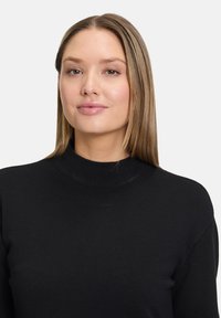Čierny rebrovaný rolák so slim fit strihom a mäkkou textúrou, s vysokým golierom a dlhými rukávmi.