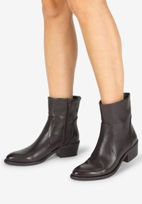 Braune Leder-Ankle-Boots mit glatter Textur, spitzer Zehenform und einem seitlichen Reißverschluss. Niedriger Blockabsatz für Stabilität und eine elegante Silhouette.