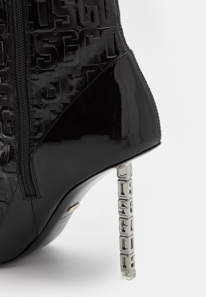 Schwarze Lackleder-Stiefelette mit geprägtem Logo-Design, seitlichem Reißverschluss und einem metallischen Blockabsatz mit gestapeltem Buchstabenmuster.