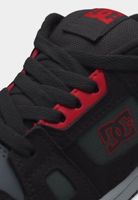 Κοντινό πλάνο στις κορδόνια παπουτσιών μαύρου και κόκκινου χρώματος, με επενδυμένη γλώσσα και το λογότυπο DC Shoes στο πλάι και στη γλώσσα του παπουτσιού.