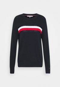 Námořnický svetr s dlouhými rukávy a kulatým výstřihem, se svislým červeným, bílým a černým pruhem přes hruď. Obsahuje texturované akcenty.