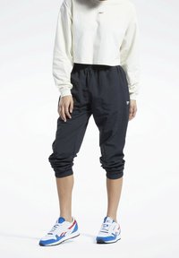 Mustat, kevyet juoksuhousut joustavilla hihanpäillä, yhdistettynä lyhytvartiseen kermaiseen huppariin. Valkoiset ja siniset urheilukengät punaisilla yksityiskohdilla.