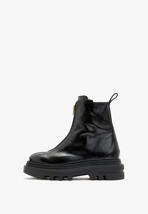 Bottine en cuir noir avec fermeture éclair avant, semelle crantée épaisse et languette de traction à l'arrière, vue de profil sur fond blanc.