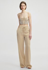Cropped beige top with intricate beading, paired with loose beige pants featuring an elastic waistband and side pockets.