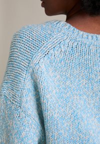 Jasnoniebieski i biały sweter dziany, z teksturowanym wzorem i szerokim dekoltem w stylu łodzi, charakteryzujący się luźnym krojem.