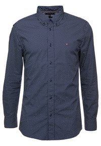 Camisa azul marino de manga larga con lunares blancos, cuello abotonado y cierre frontal con botones. La tela parece suave con un ligero brillo.