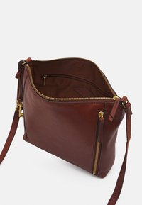 Brun læder håndtaske med en tekstureret overflade, guld hardware, top lynlås og justerbar rem. Har indvendig lomme og sidelukning med lynlås.