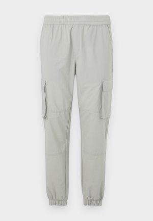 Světlé šedé cargo kalhoty s elastickým pasem, zúženými kotníky, dvěma bočními kapsami a dvěma velkými postranními cargo kapsami. Hladká textilie.