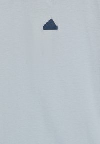 Jasnoniebieska bawełniana koszulka z okrągłym dekoltem, z ciemnoniebieską łatką z logo Adidas na lewej piersi. Gładka struktura, prosty design.