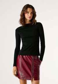 Μαύρο μακρυμάνικο τοπ με ριμπ ύφανση, συνδυασμένο με γυαλιστερή μίνι φούστα σε βαθύ μπορντό χρώμα με πλευρικό φερμουάρ και τσέπες.