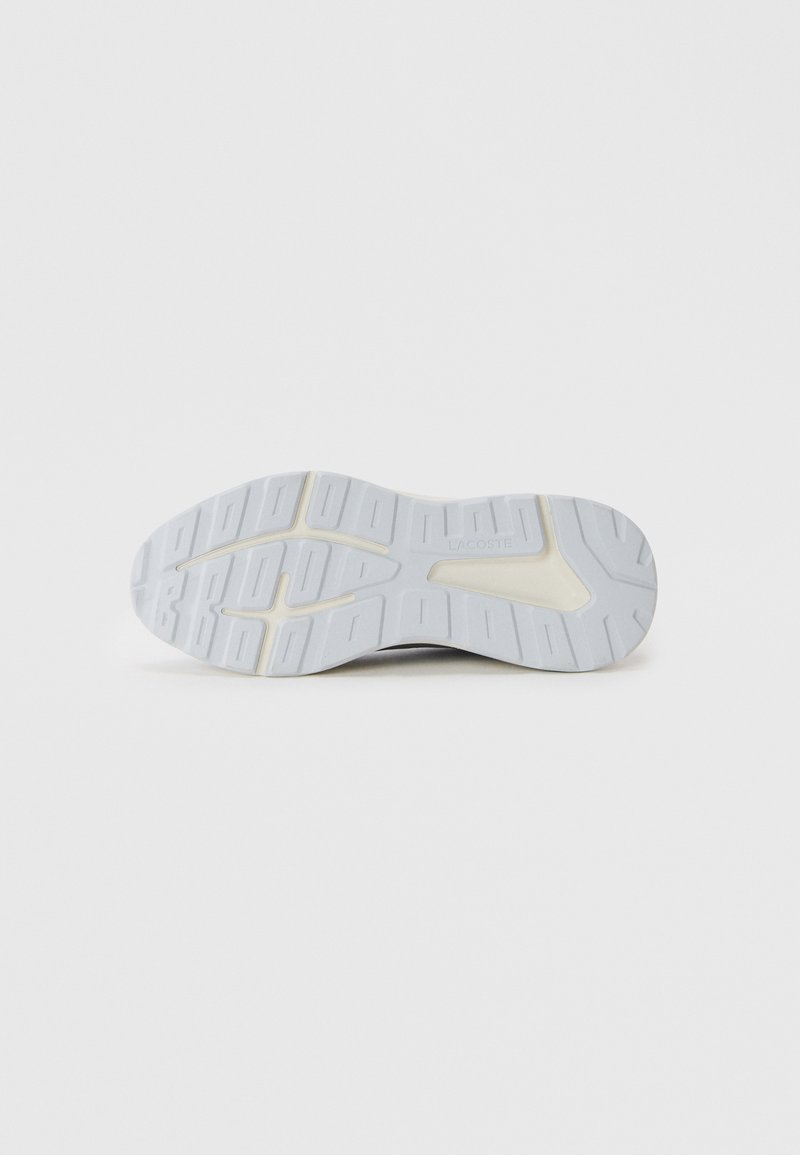 Semelle d'une chaussure de sport blanche avec des motifs en relief rectangulaires et le nom de la marque "Lacoste" embossé près de l'arche.