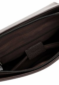 Interno di borsa in pelle marrone scuro con tasca con cerniera, fodera in tessuto e una piccola etichetta in pelle cucita all'interno.