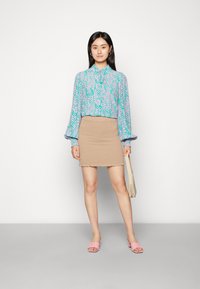 Blusa de manga longa em roxo claro com padrões abstratos em verde-azulado, combinada com uma saia mini texturizada em bege e sandálias de dedo rosa.