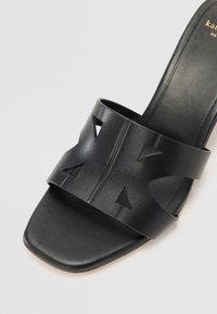 Sandalo nero con una larga fascia caratterizzata da disegni a triangolo ritagliati. Texture in pelle liscia, punta quadrata e tallone aperto. Design minimalista.