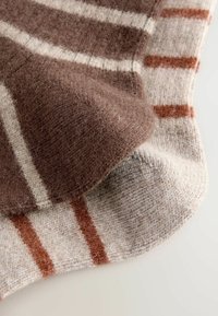 Coperta in lana a strisce marroni e beige con una texture morbida, caratterizzata da strisce larghe e strette in colori alternati, adagiata piatta.